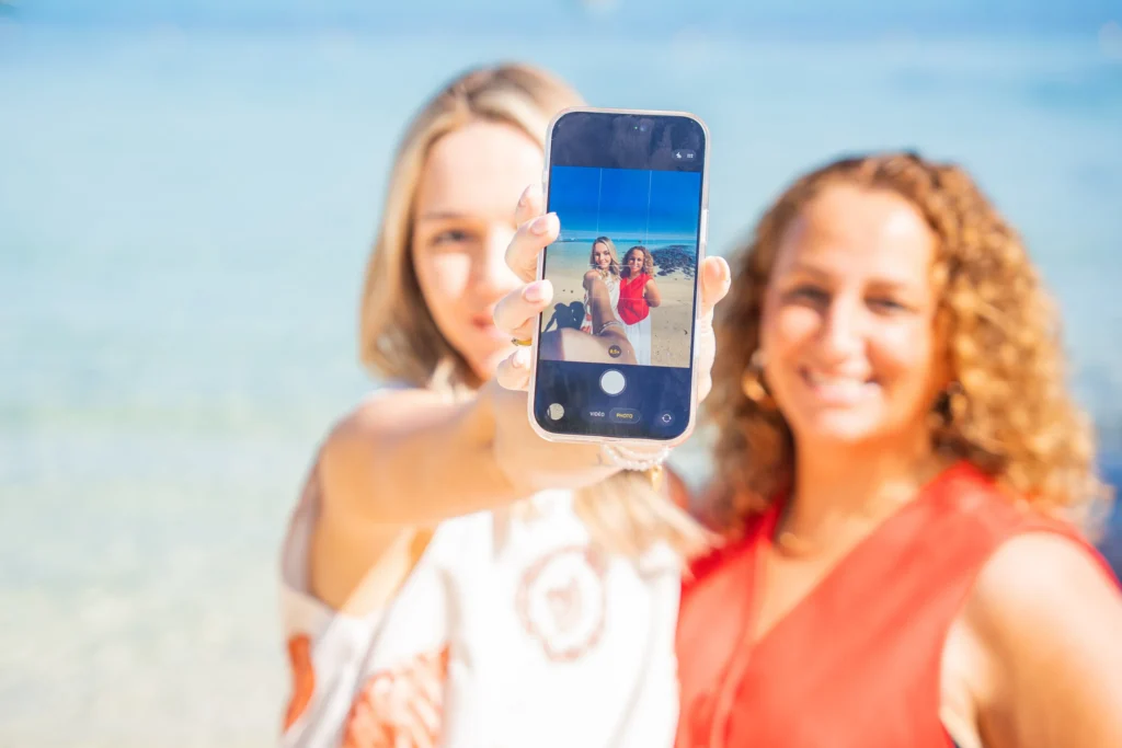 Deux femmes souriantes prenant un selfie sur une plage ensoleillée